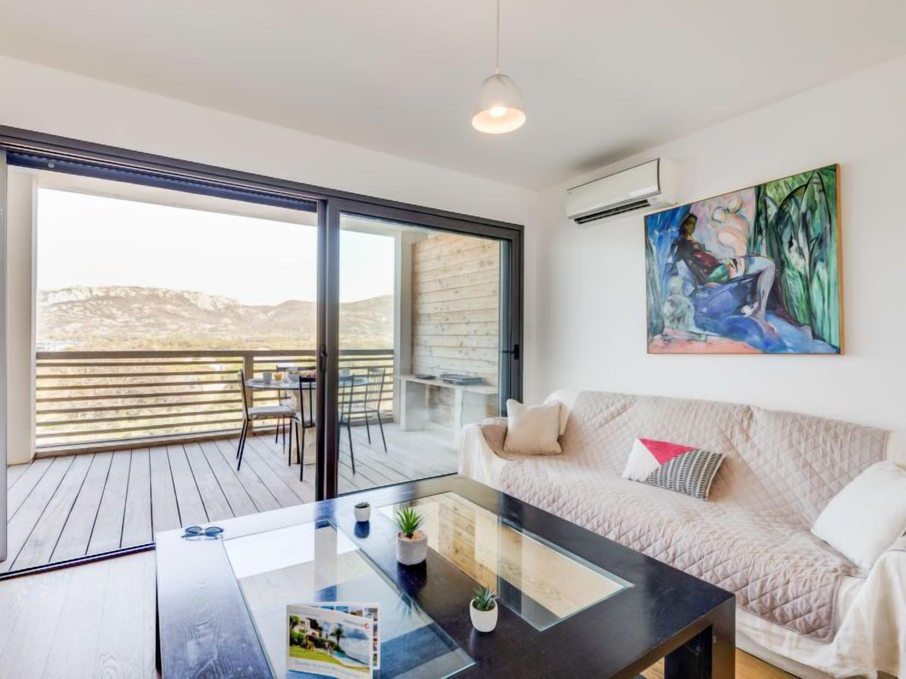 Uma sala de estar moderna com uma mesa de centro de vidro, um sofá e uma varanda com vista para as montanhas.