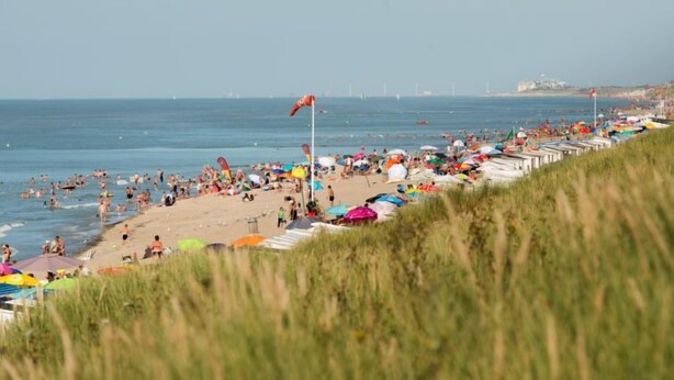 Een strand met rijen strandparasols en tenten, een zandstrand en de zee op de achtergrond.