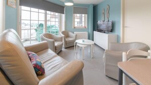 Een moderne woonkamer met een bank, stoelen, een klein tafeltje en een televisie.