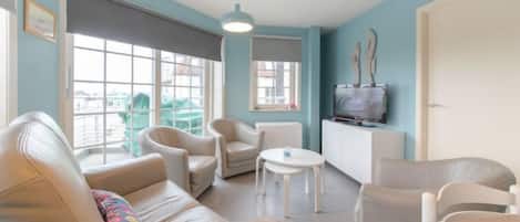 A modern living room with a sofa, chairs, a small table, and a television.