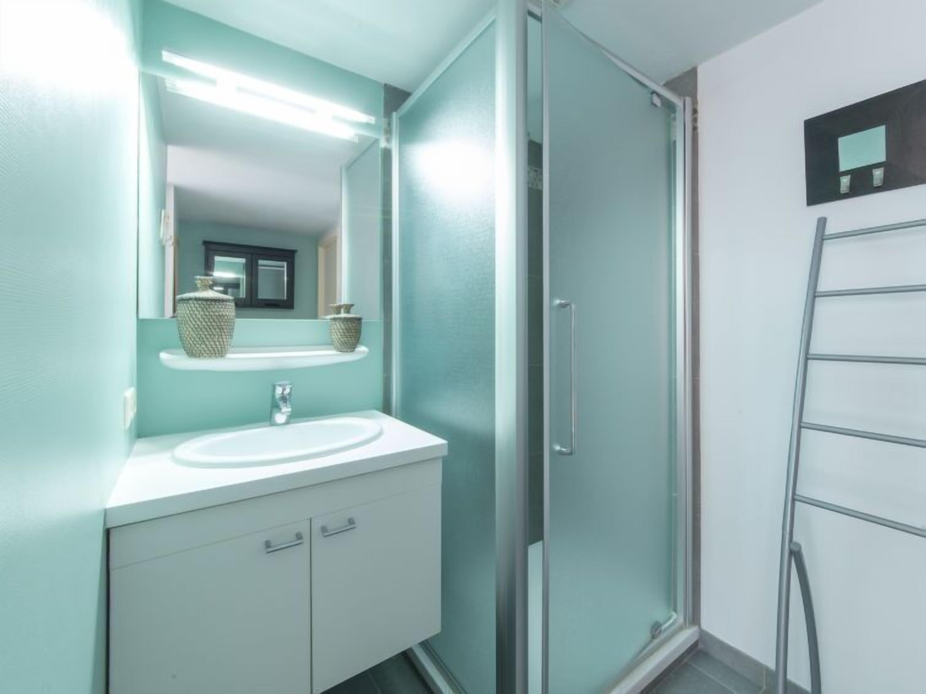 Un bany amb un lavabo blanc, un mirall i una cabina de dutxa.
