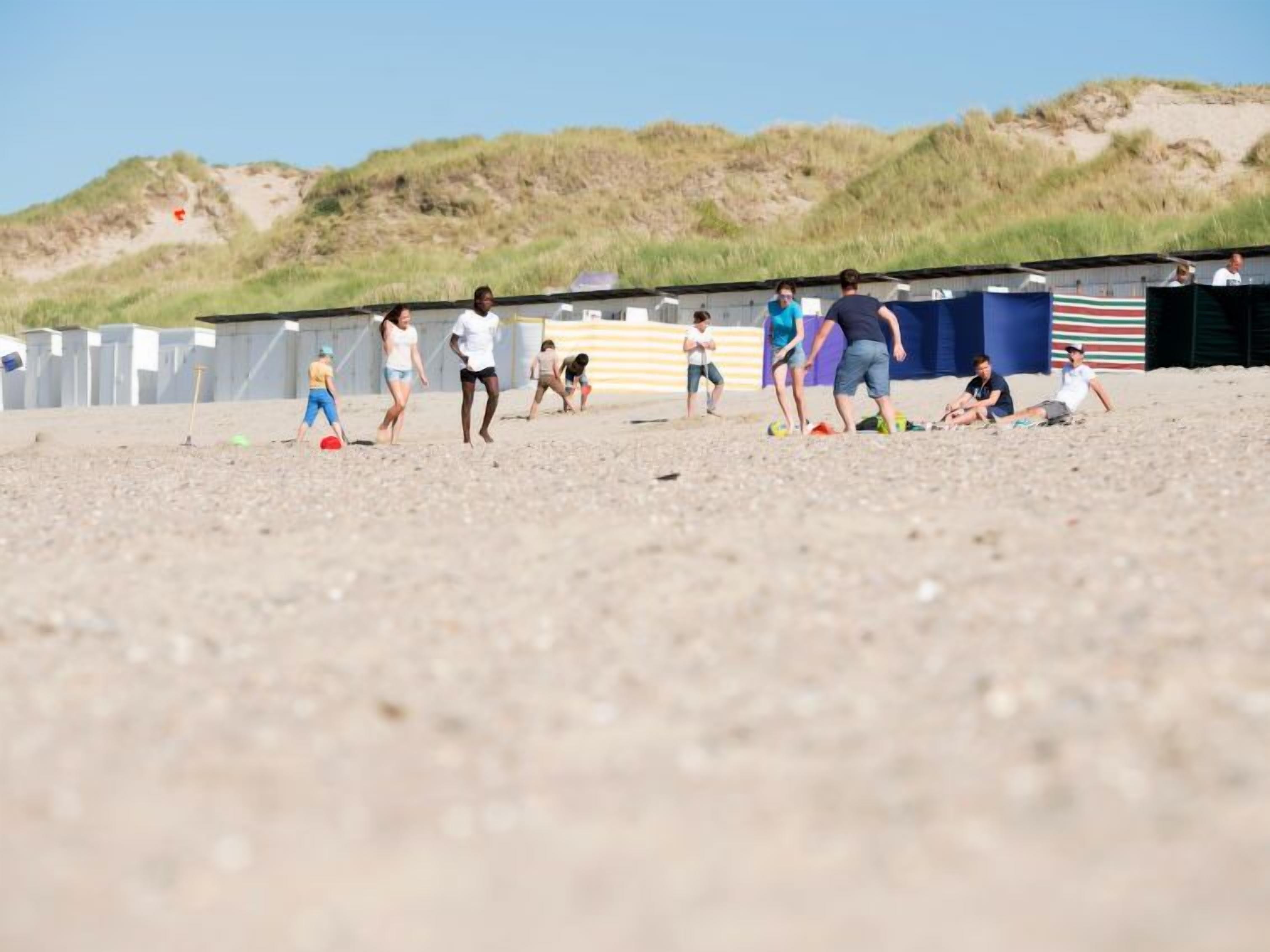 A beach with people playing and a structure in the background.