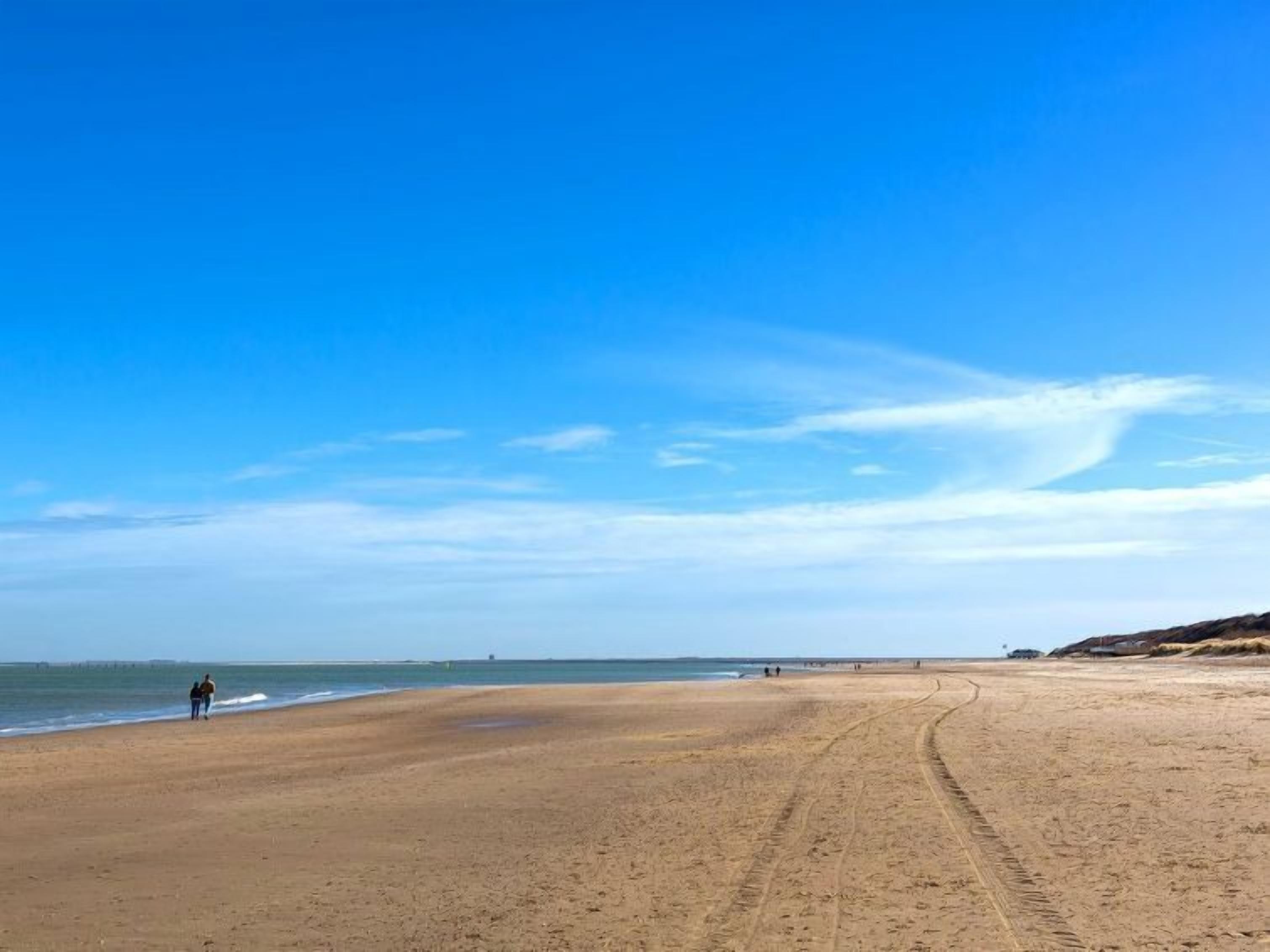 A wide sandy beach with a clear blue sky and a distant pier.