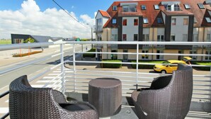 Een balkon met rieten stoelen en uitzicht op een meerverdiepingsgebouw met een rood dak.