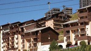 A multi-story hotel with balconies, ski lift cables, and a mountainous backdrop. - Astragale 412 A by Interhome (Les Menuires)