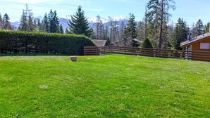 A grassy outdoor area with a wooden fence, a wooden cabin, and a mountain backdrop. - Santa Barbara 23 by Interhome (Crans-Montana)