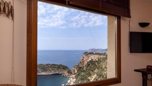 A room with a large window overlooking a coastal landscape, a television mounted on the wall, and a wicker chair. - Vacation home Igor by Interhome (Jávea)