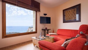 A living room with a red sofa, a glass coffee table, a TV, and a view of the ocean. - Vacation home Igor by Interhome (Jávea)