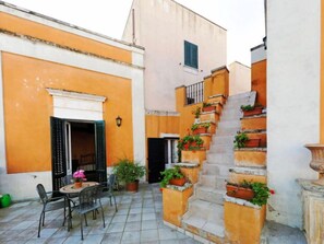 A courtyard with a tiled floor, a table with chairs, and a staircase with potted plants.