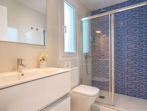 Ein modernes Badezimmer mit einem weißen Waschbecken, einer Toilette und einer Duschkabine mit blauen Mosaikfliesen.