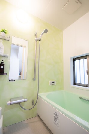 A bathroom with a shower, a bathtub, a toilet, a mirror, and a window. - AMP FLAT Haruyoshi A (Fukuoka)