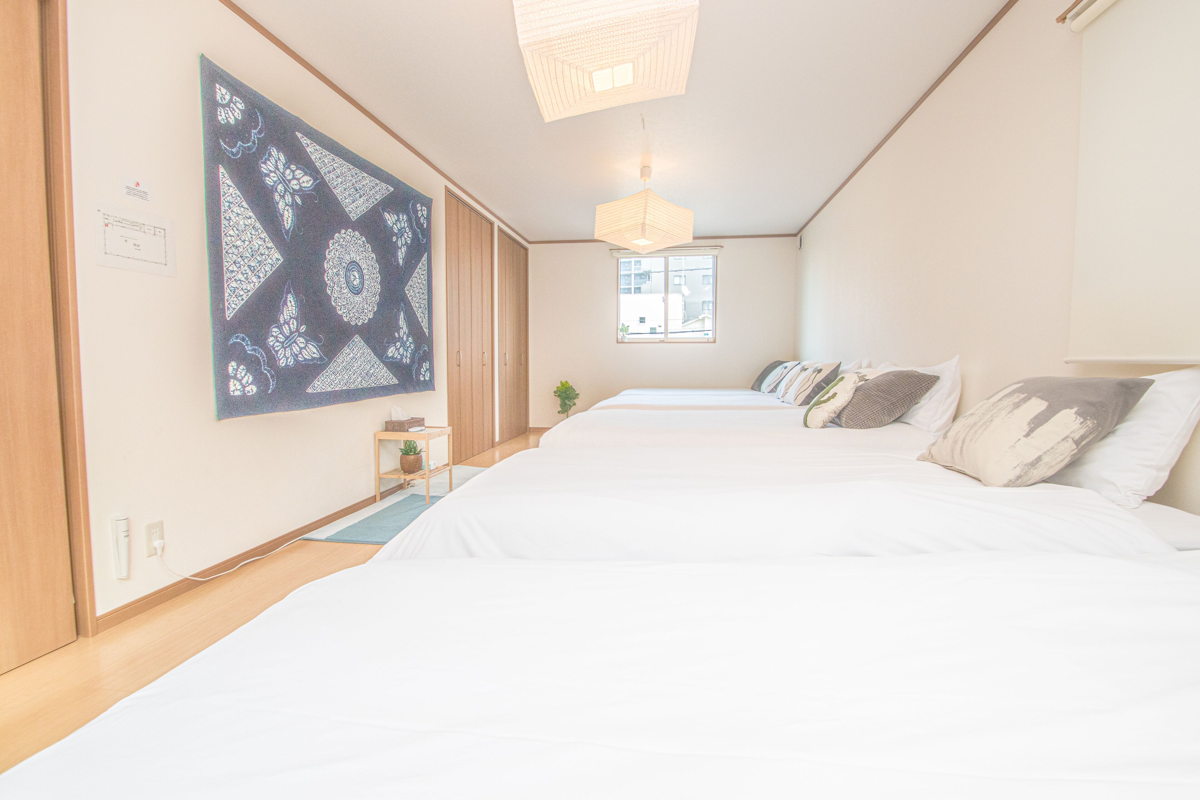 A hotel room with a large bed, a wall-mounted artwork, a window, and a hanging light fixture.