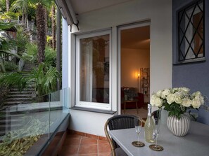 A balcony with a glass railing, a dining table with chairs, a vase of flowers, and a bottle. - Junior Suite Classic by Interhome (Ascona)