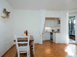 A compact kitchen with white cabinets, a wooden dining table, and a white chair. - Junior Suite Classic by Interhome (Ascona)