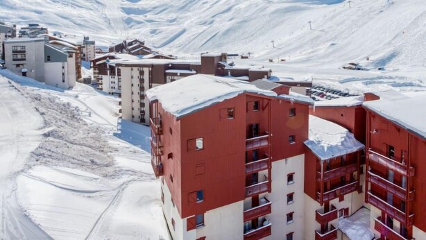Een bergstad bedekt met sneeuw, met meerlaagsgebouwen, waaronder een opvallend rood gebouw met balkons.