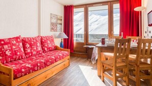 Een gezellige kamer met een houten bank, een eettafel met stoelen en uitzicht op besneeuwde bergen door grote ramen.