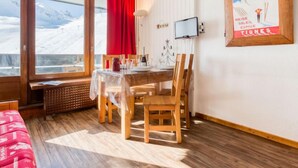 Een eetruimte met een tafel voor twee personen, een aan de muur bevestigde televisie, en een raam met uitzicht op besneeuwde bergen.