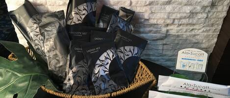 En kurv fyldt med tasker i sort-hvide mønstre, mærket "LADIES SET INNOVATE" og "RAZOR BRUSH INNOVATE", foran en struktureret væg.