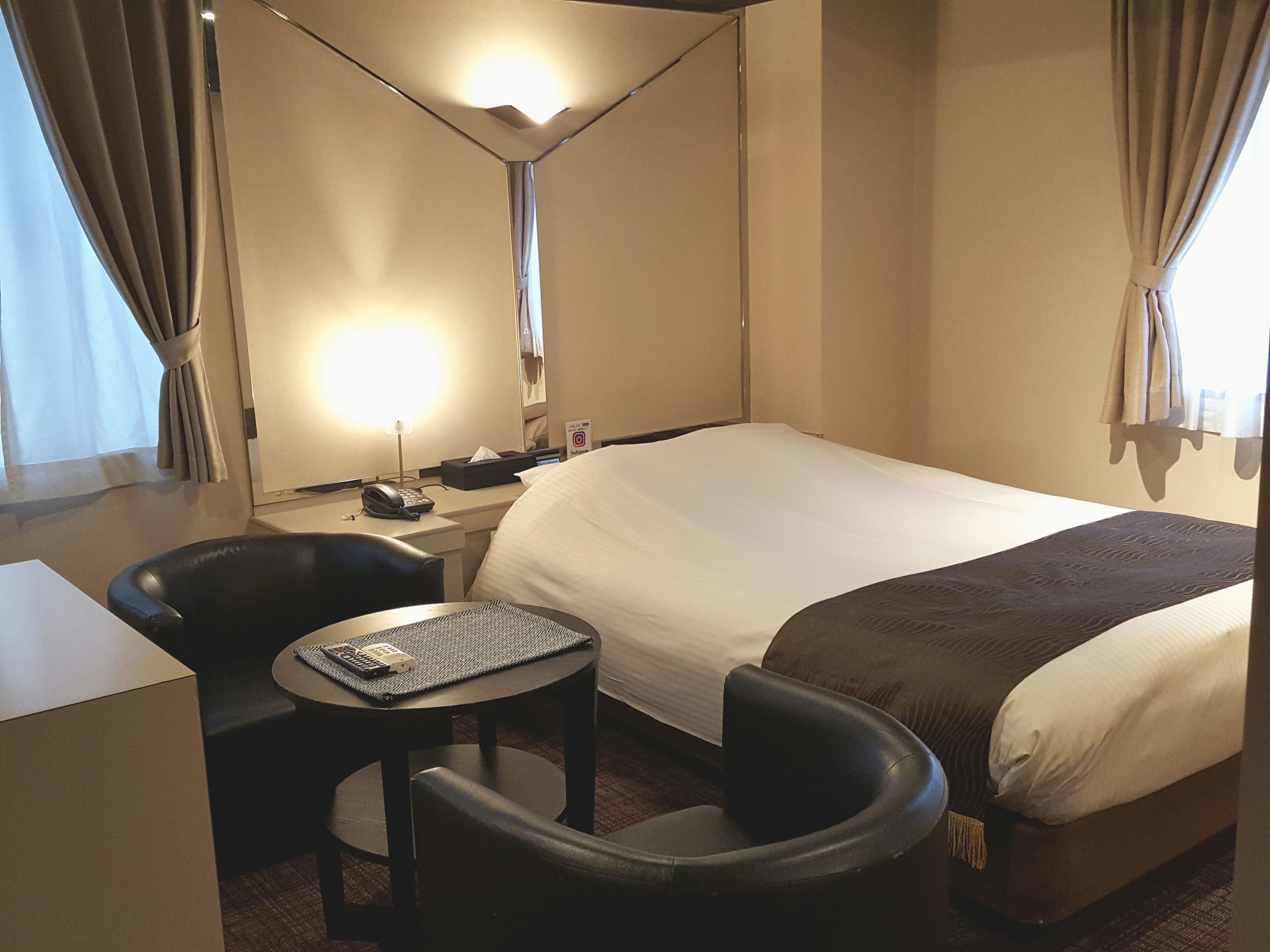 Una habitació d'hotel amb un llit, una taula de nit amb telèfon, una cadira, una taula rodona petita i una làmpada.
