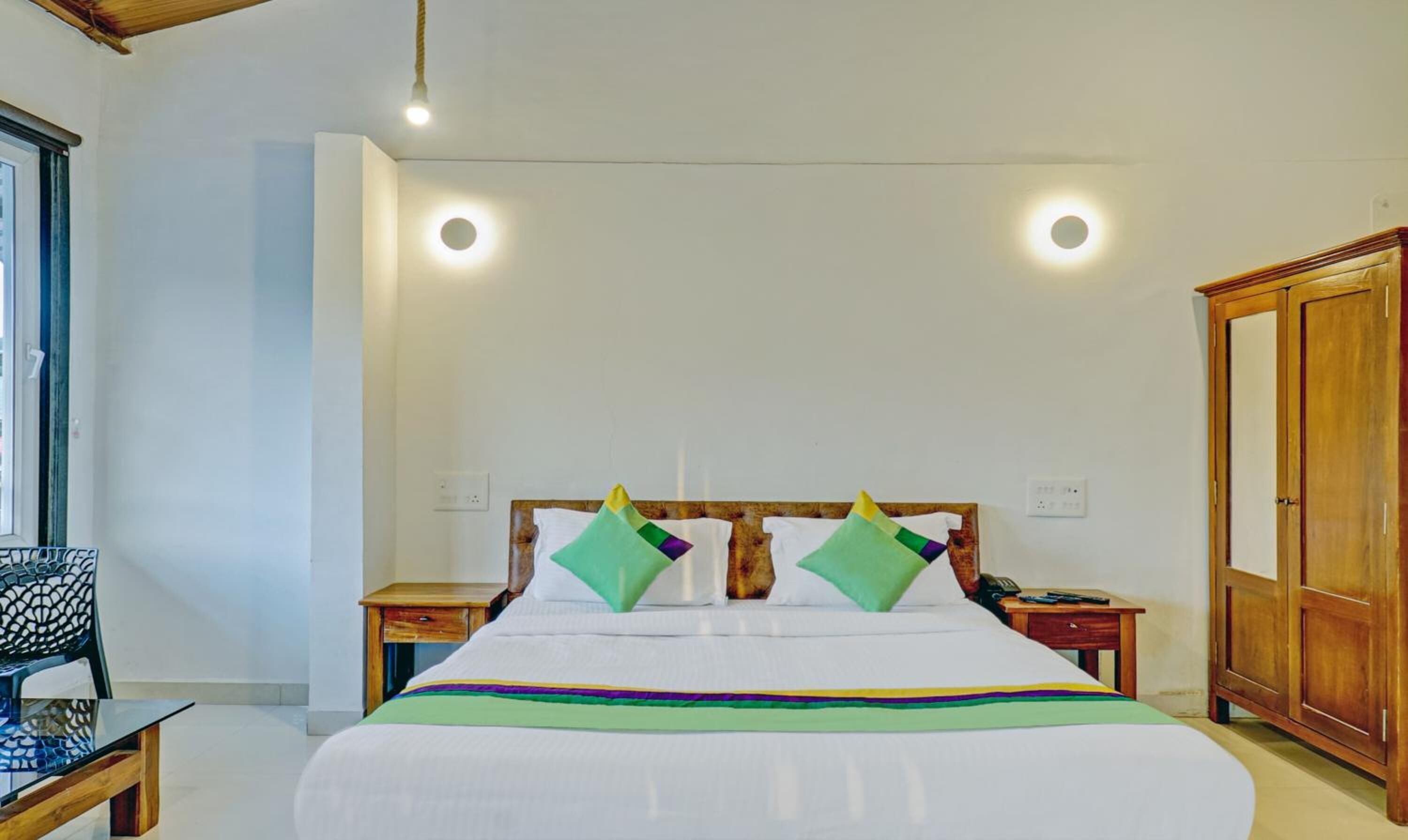 A hotel room with a large bed, two bedside tables, a wooden wardrobe, and a chair.