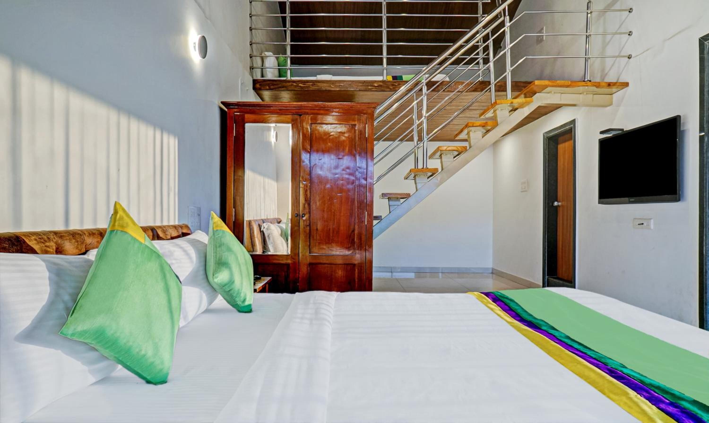 A bedroom with a bed, pillows, a wooden door, a staircase, and a TV.