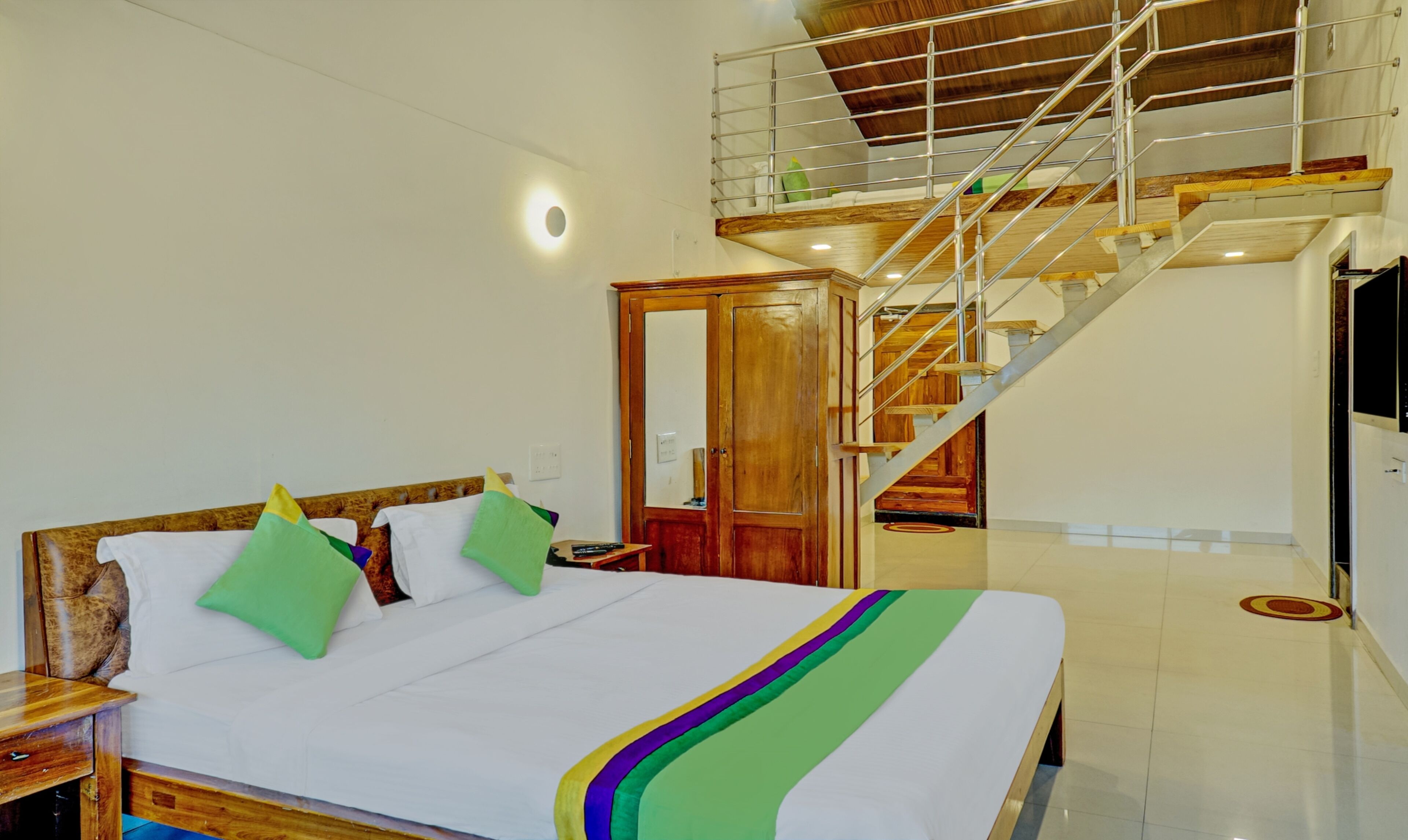 A bedroom with a bed, wooden headboard, and a staircase leading to an upper level.
