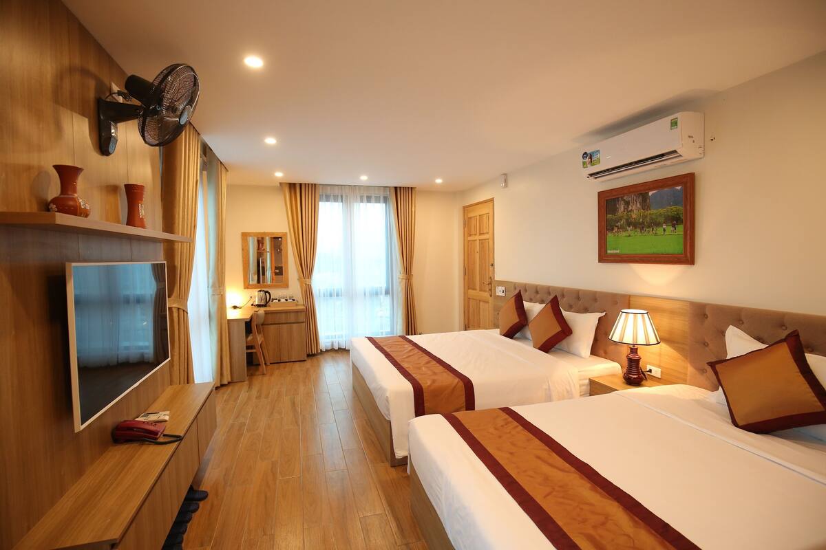A hotel room with two beds, a TV, a desk, and a bathroom.