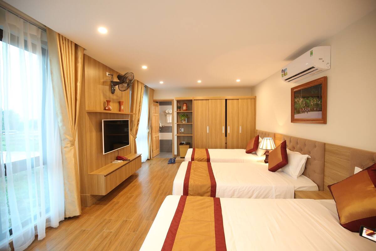 A hotel room with three beds, a TV, a wardrobe, and a window with curtains.