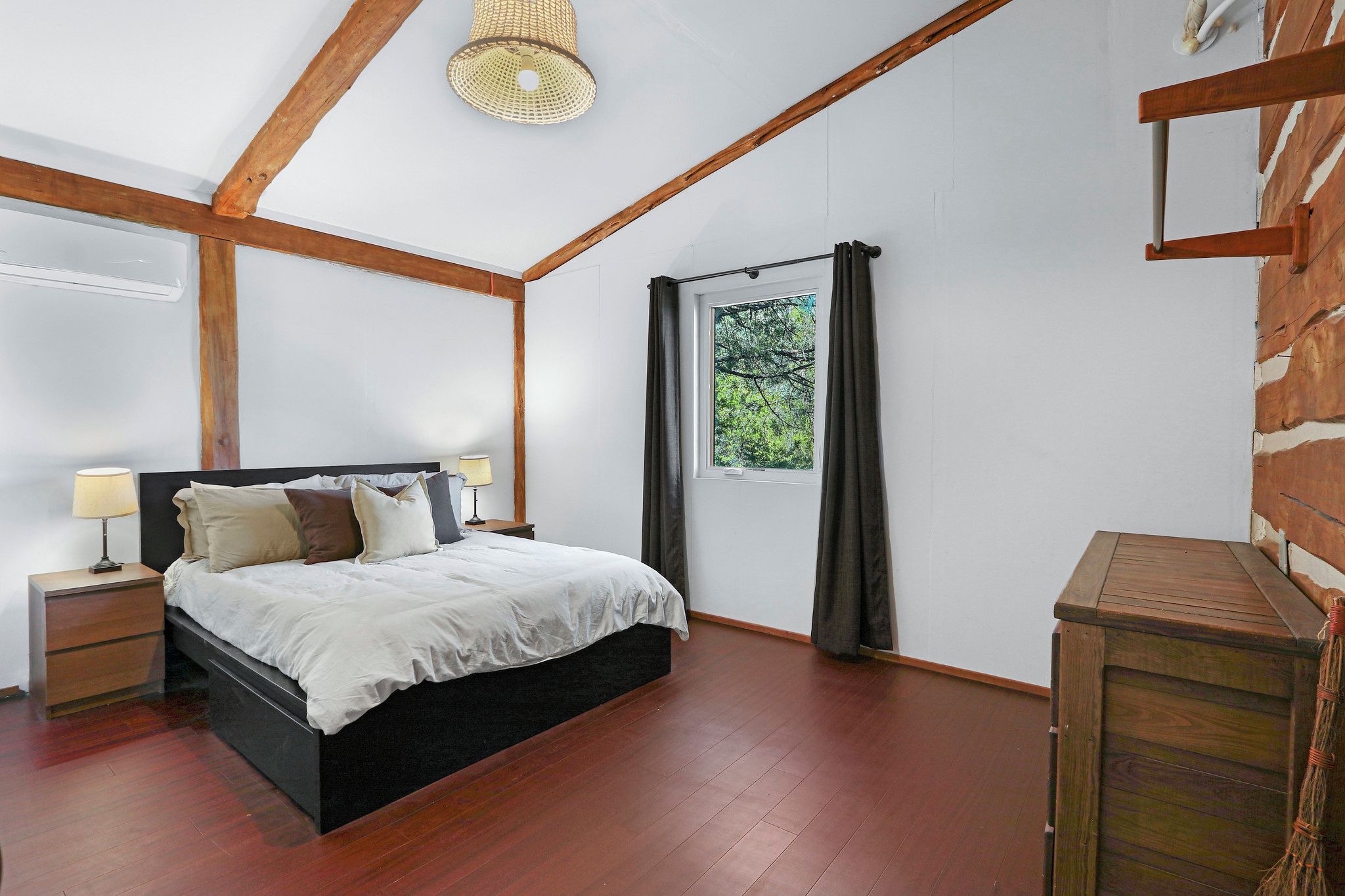A bedroom with a bed, nightstands, a window with curtains, and a wooden ceiling.