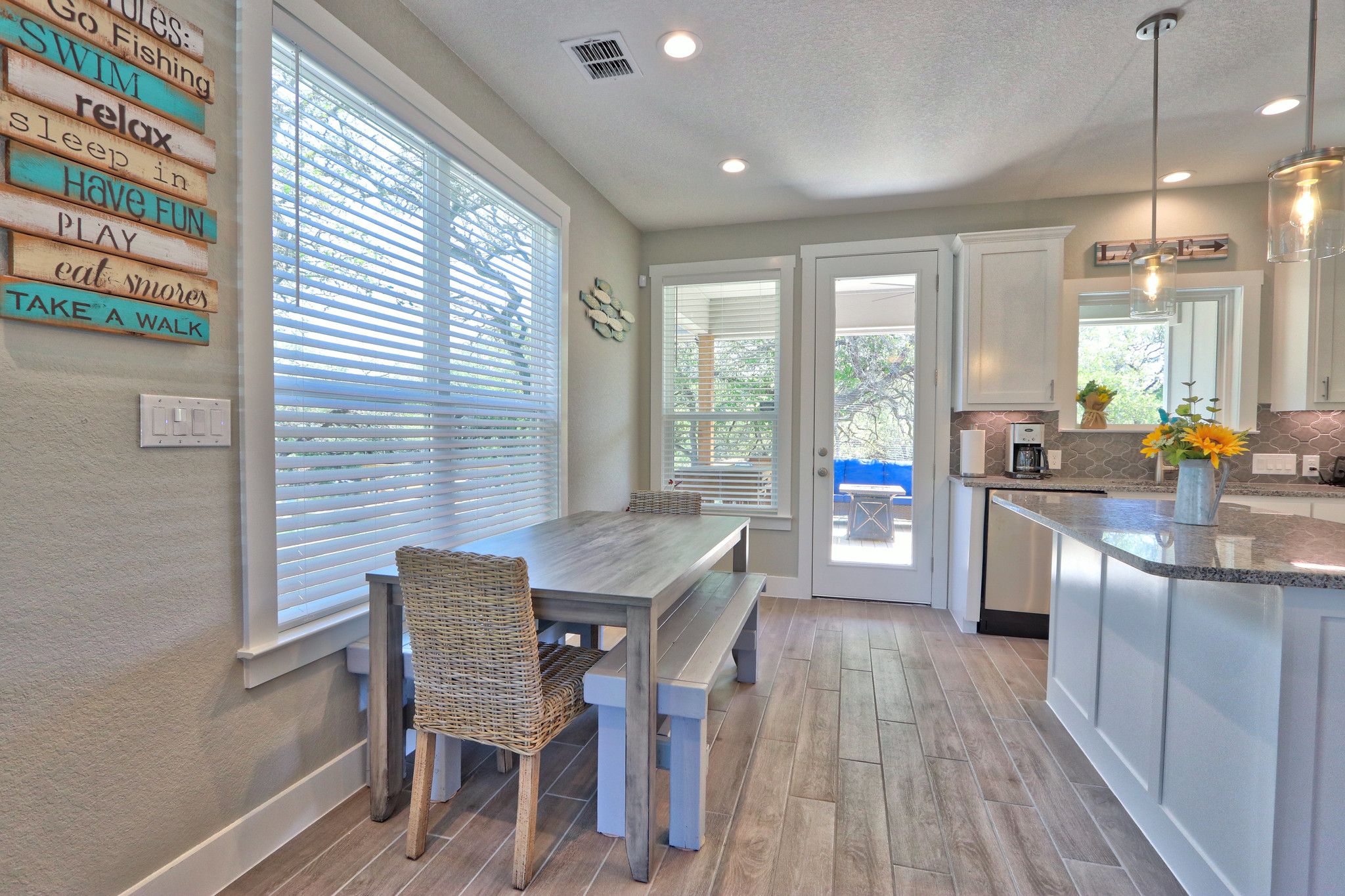 A modern kitchen with a dining area, featuring a wooden table and chairs, a built-in island with a sink, and a view through the window.