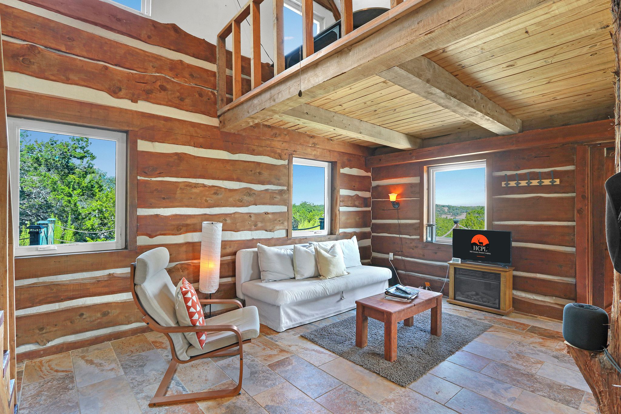 Interior de una cabaña de troncos con un sofá, un sillón y una chimenea.