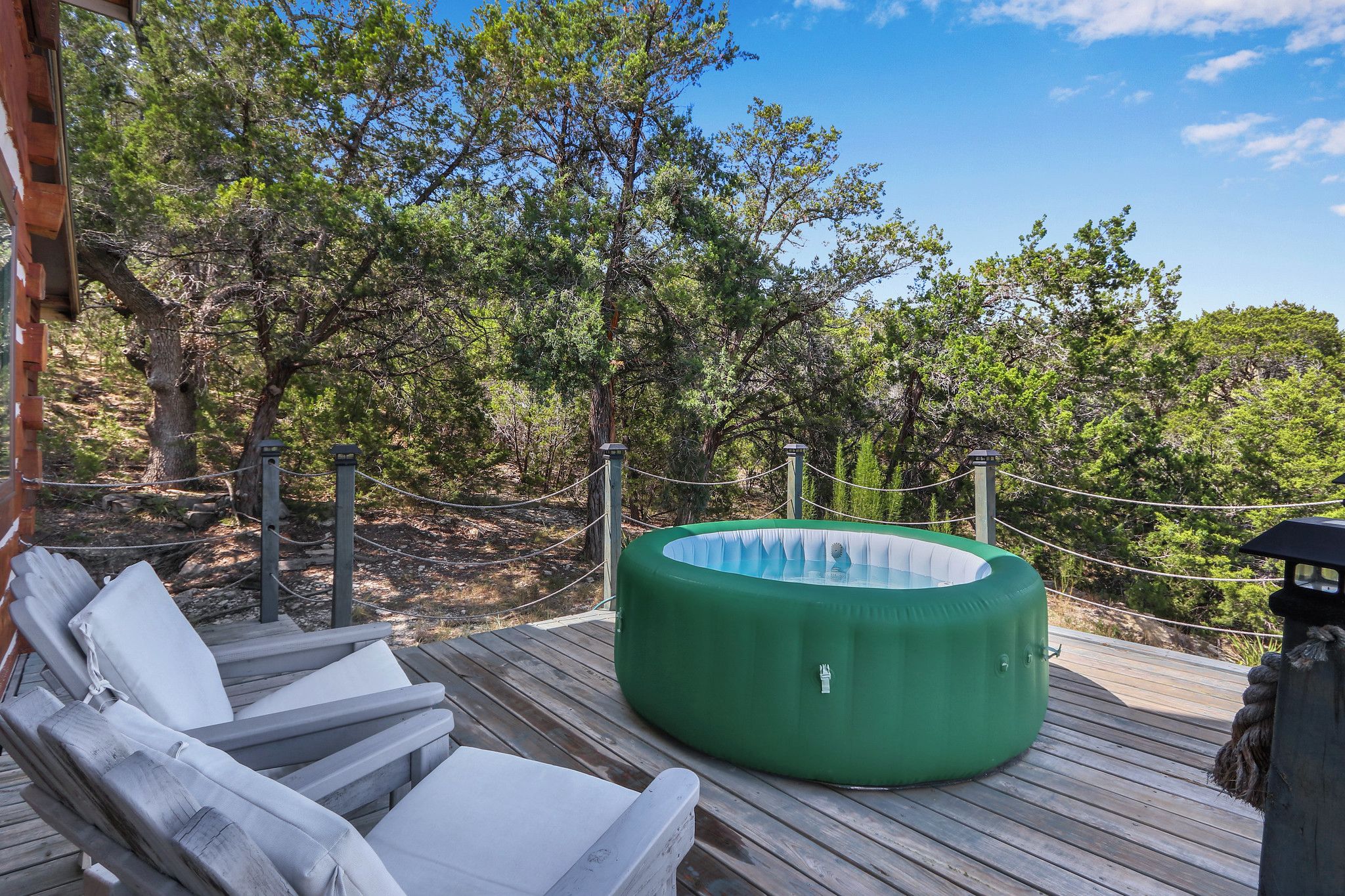 A wooden deck with lounge chairs and a green hot tub.
