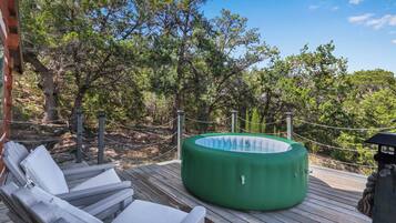 A wooden deck with lounge chairs and a green hot tub.