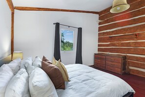 A bedroom with a bed, pillows, a dresser, a window with curtains, and a wooden wall.