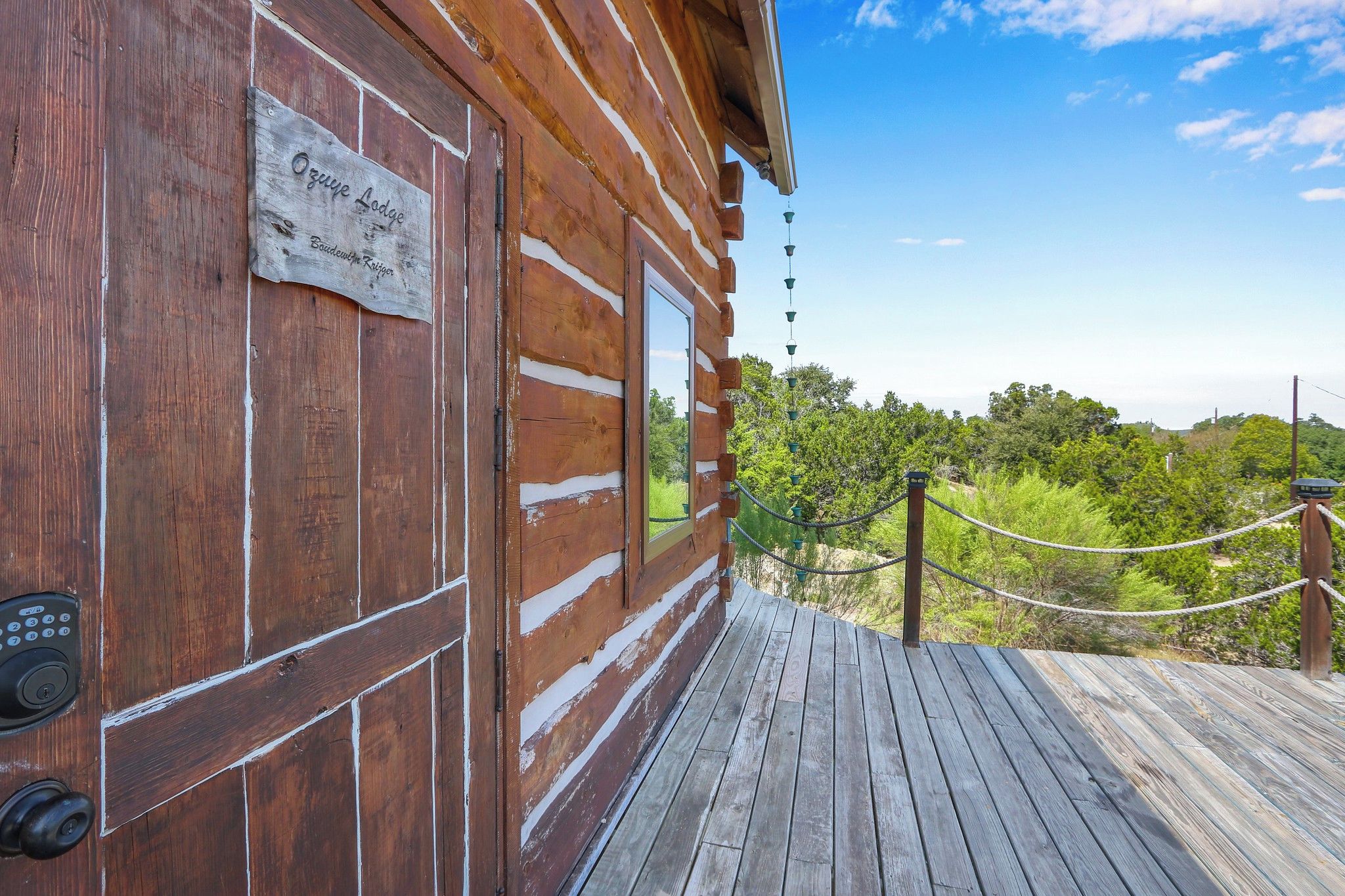A wooden cabin with a sign reading 'Ozye Lodge' and a wooden deck leading to a scenic view.