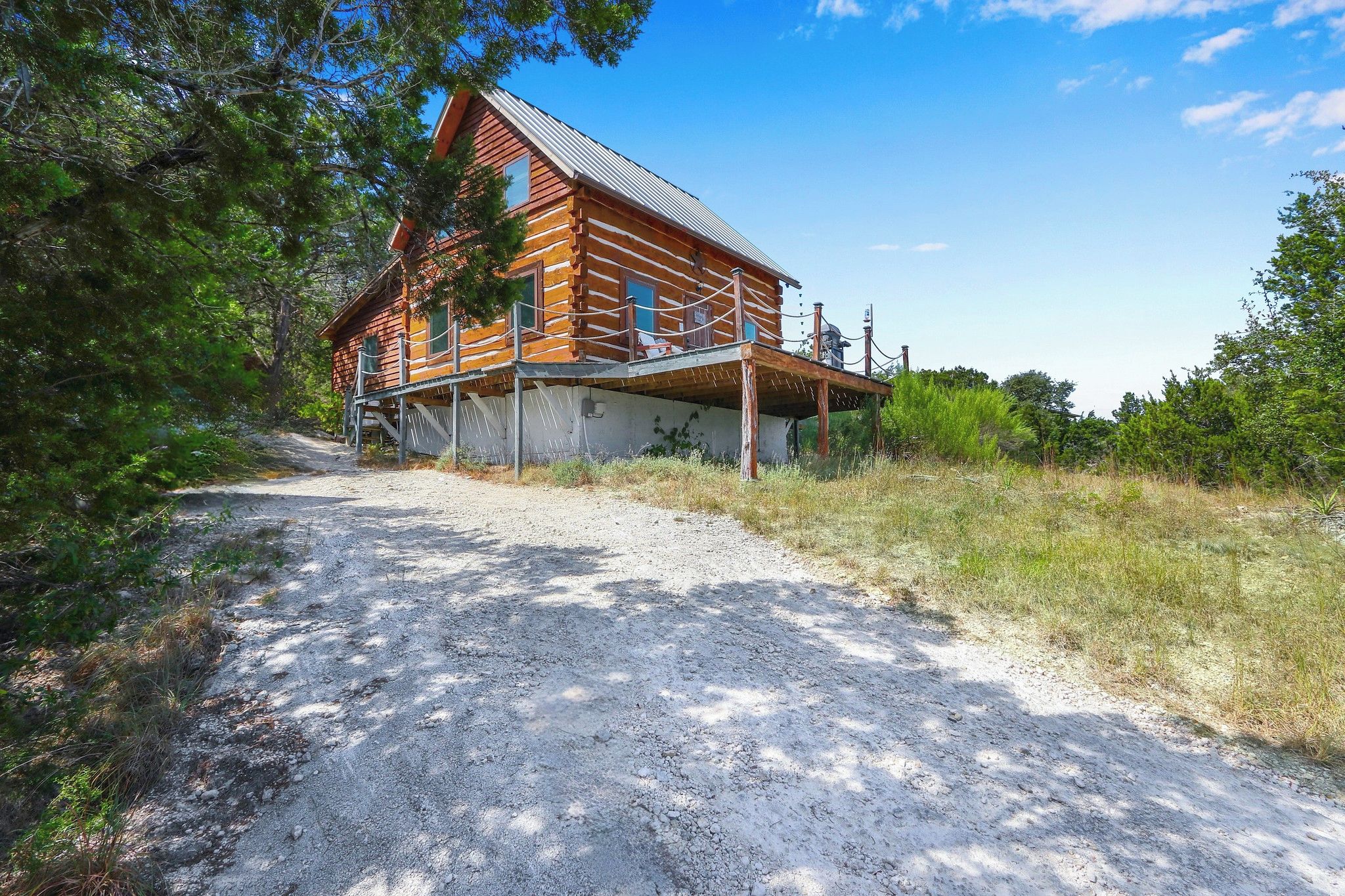 A wooden cabin with a metal roof, surrounded by trees and a gravel path.
