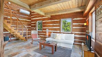 A log cabin interior with a staircase, a sofa, a coffee table, and a television.