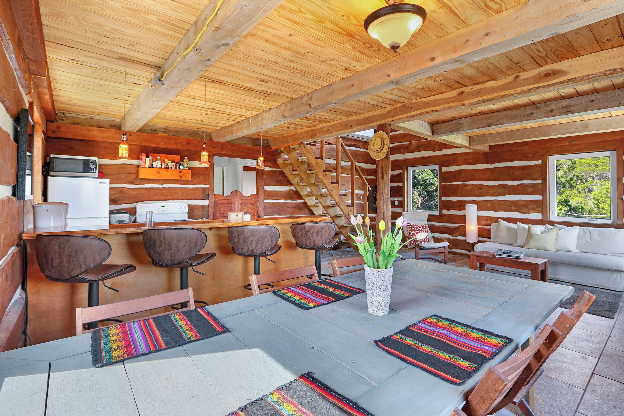 A wooden cabin interior with a dining area, kitchen, and seating space.