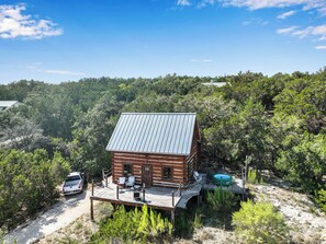 A wooden cabin with a metal roof, surrounded by dense forest, and a small pool area.