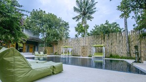 A swimming pool with a green cushioned seating area, a bamboo fence, and tropical plants. - Villa 6# 1BR Stunning Villa w/ Public pool at downtown Ubud (Ubud)