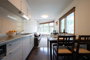 A modern kitchen with white cabinets, a dining area with a table and chairs, and a large window providing natural light. - Yukon (Kutchan)