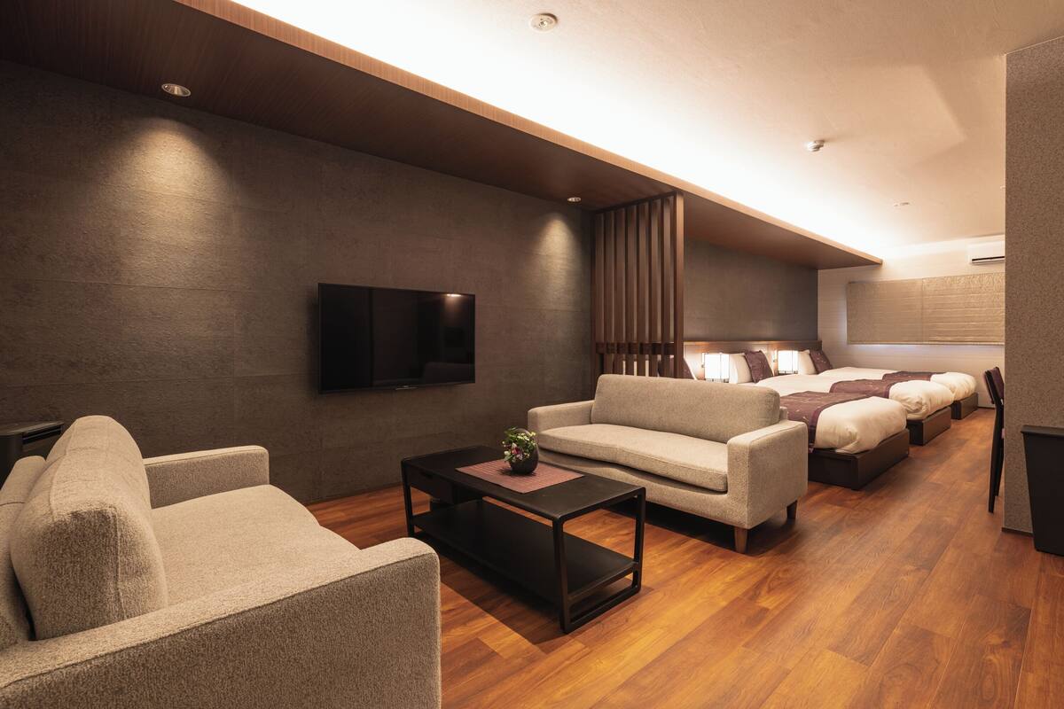 A modern living room with a sofa, a coffee table, a TV, and a bed with a headboard.