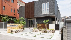 A modern two-story building with a stone entrance, a wooden slatted wall, and a sign reading "Grand Base Iolani". - GRAND BASE Iolani (Beppu)