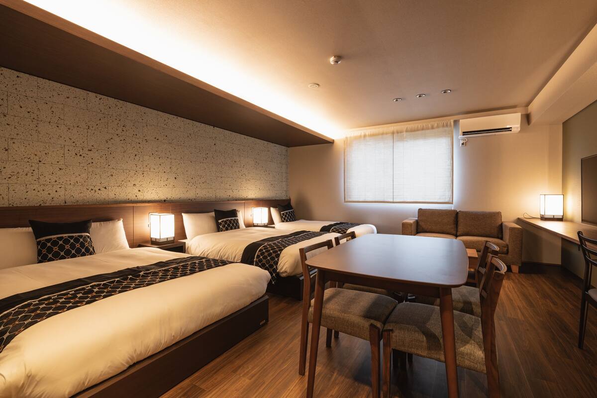 A hotel room with three beds, a dining table, and a TV.