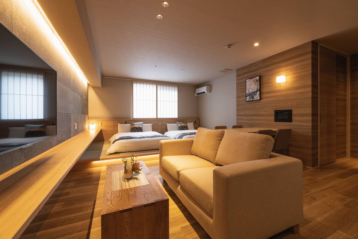 A modern hotel room with a large bed, a sofa, a wooden coffee table, and a large mirror.