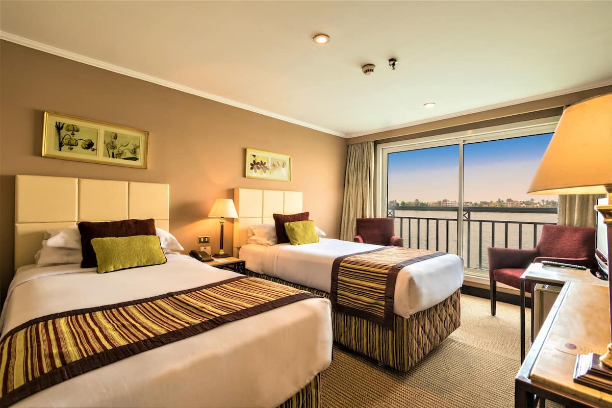 A hotel room with two beds, a desk, a chair, and a large window with a view of the city.