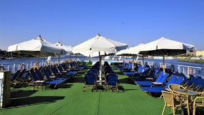 Una terraza con hileras de sillones azules y sombrillas blancas, con vista a un cuerpo de agua.