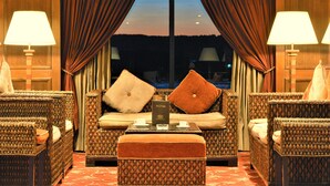 A hotel room with a sofa set, two armchairs, a coffee table, and a view of the night sky. - JAZ Crown Jubilee Nile Cruise - Every Thursday from Luxor for 07 & 04 Nights - Every Monday from Aswan for 03 Nights (Luxor)