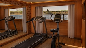 Un gimnasio con cintas de correr y una máquina elíptica, ventanas amplias con vista a un cuerpo de agua, y paneles de madera.