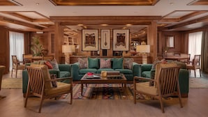 Un salón amplio con un sofá verde, sillas de madera, una mesa de centro y obras de arte enmarcadas en las paredes.